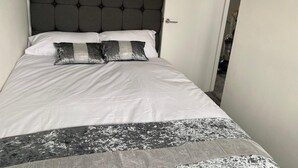 A neatly made bed with a dark headboard, white bedding, and two decorative pillows.