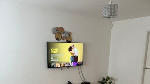 A living room with a flat-screen TV mounted on the wall, a wooden entertainment unit below, and a potted plant on the floor.