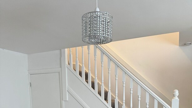 A living room with a grey sofa, a white staircase, and a crystal chandelier.
