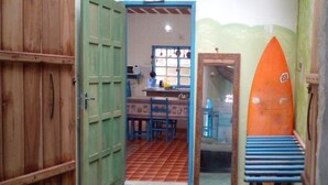 A narrow hallway with a wooden door, a tiled floor, and a surfboard leaning against the wall. - Casa da Piscina 3 bed House Near to the Beach (Saquarema)
