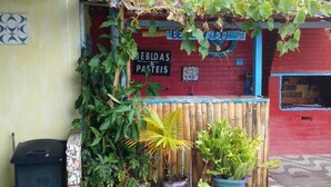 A storefront with a red brick wall, a sign reading "BEBLIDAS & PASTES," and various potted plants in front. - Casa da Piscina 3 bed House Near to the Beach (Saquarema)