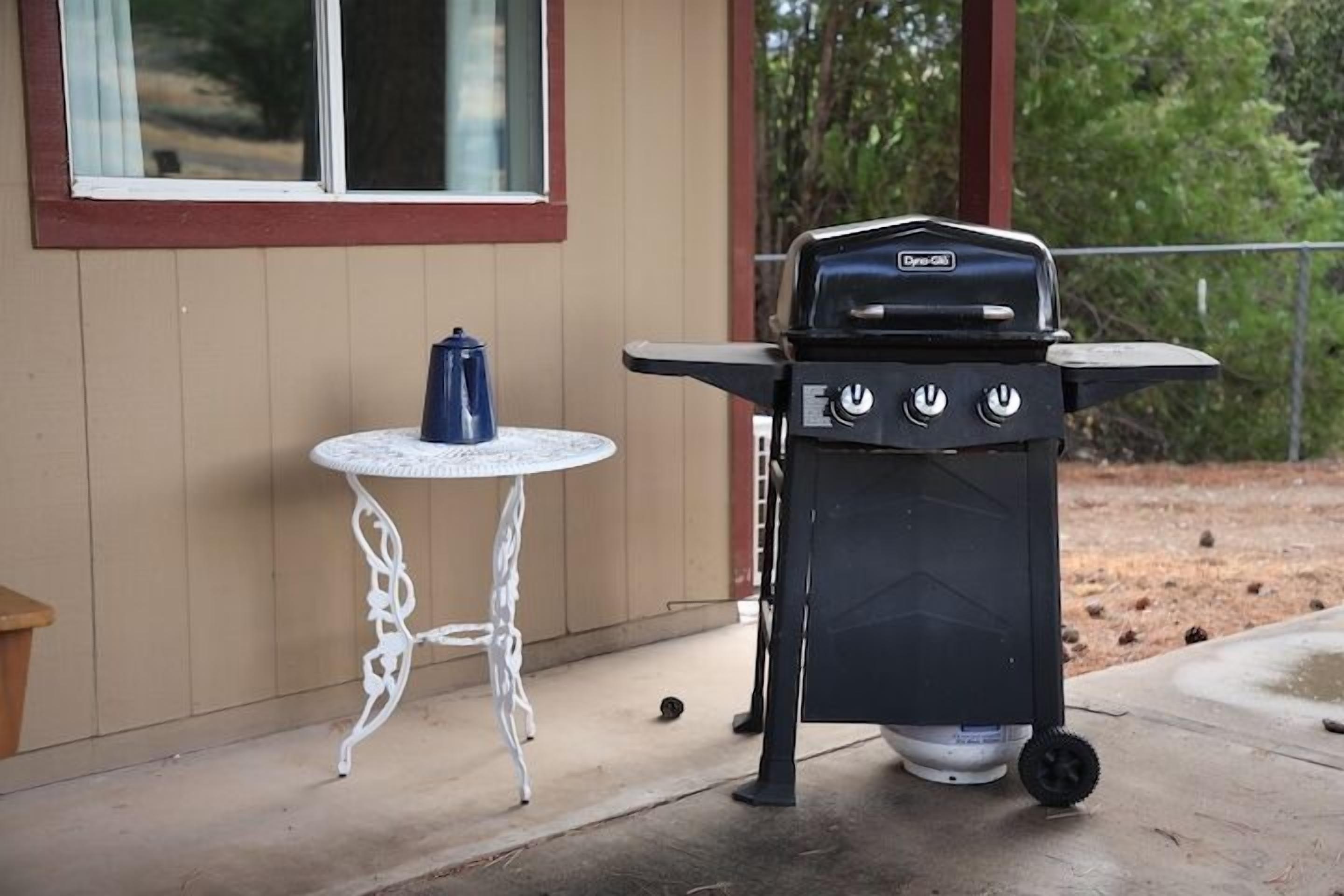 Una parrilla portátil con tanque de gas y una pequeña mesa con un contenedor azul a su lado.