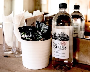 Una botella de agua Purely Sedona, una taza blanca con bolsitas de té y un vaso.