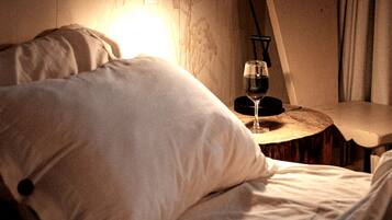 Een bed met een kussen, een nachtkastje met een glas wijn en een lamp.