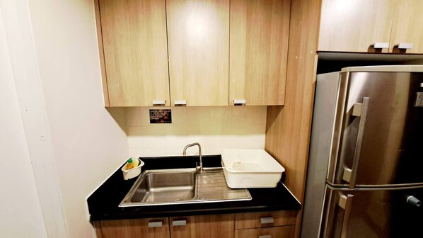 A compact kitchen with wooden cabinets, a stainless steel sink, and a refrigerator. - 5B - Short-Term Rental Allowed - Downtown Bkk Serviced Apartment (Krung Thep Maha Nakhon)