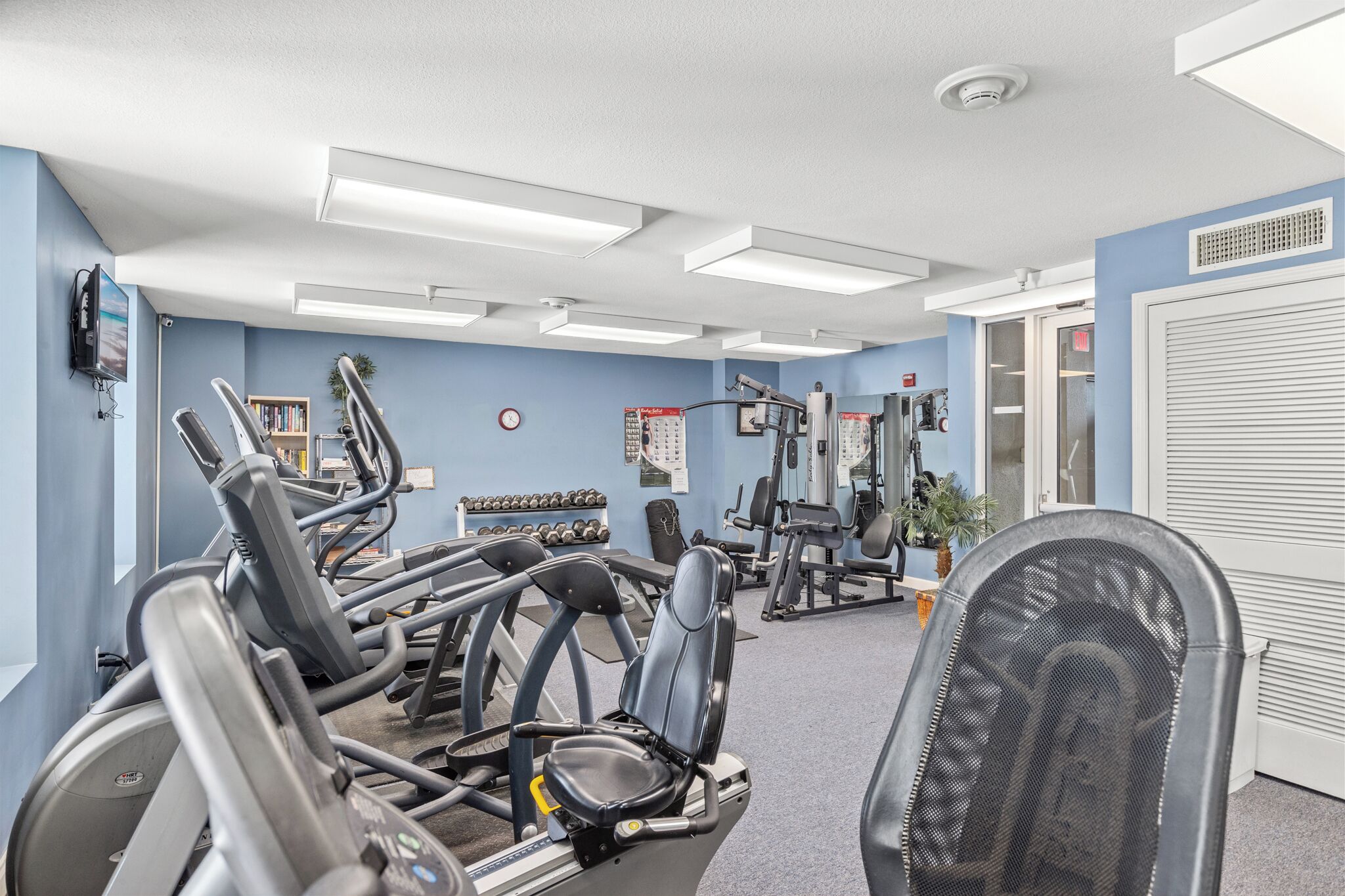 Ein Fitnessraum mit Laufbändern, Kraftgeräten und einem Stuhl.