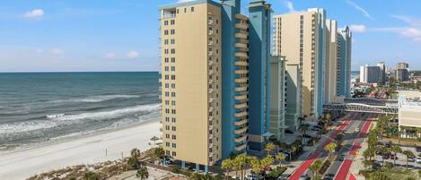 A coastal high-rise building with a beach view, a pedestrian walkway, and a red bike lane.