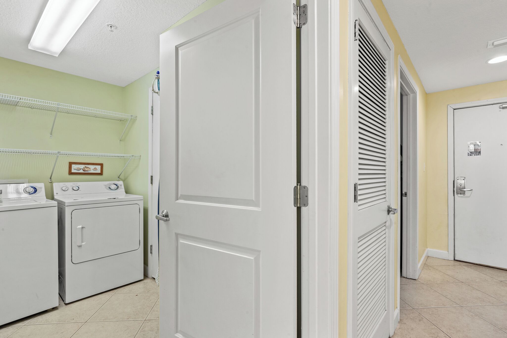 A laundry room with two washers and dryers, a door, and a wall-mounted shelf.