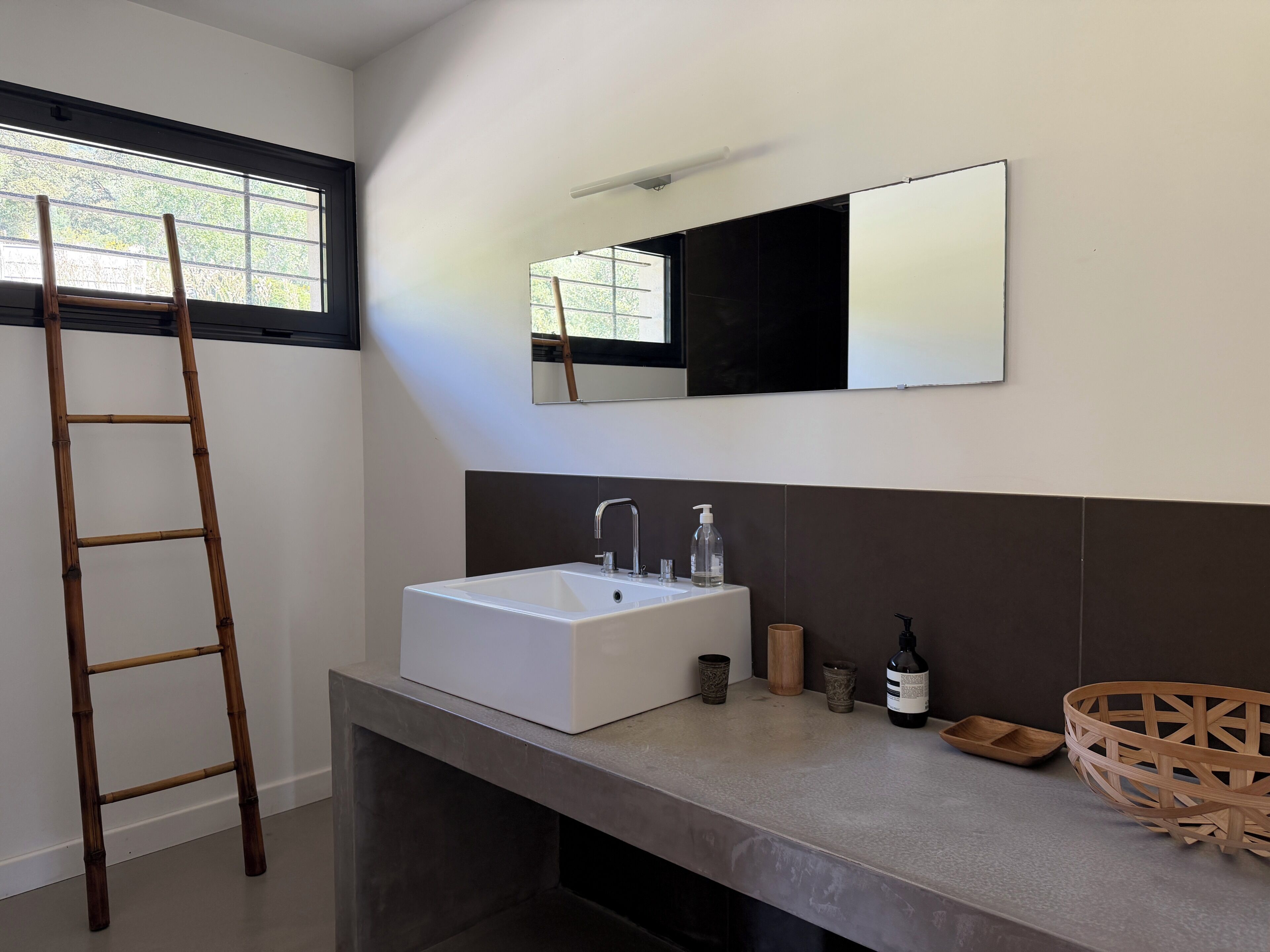 A modern bathroom with a large sink, mirror, and a wooden ladder.