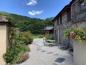 A gravel path leading to a stone building with a wooden bench and a hanging flower basket. - Charming 1-bed Cottage in Liskeard Cornwall (Liskeard)