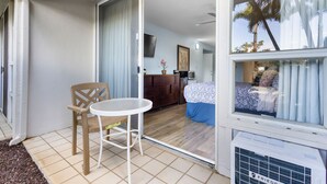 Habitació amb llit, escriptori, cadira i una porta corredissa de vidre que dona a un balcó.