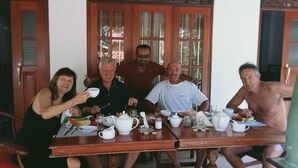 A group of people seated around a wooden table with various dishes and utensils. - Charika Villa (Bentota)