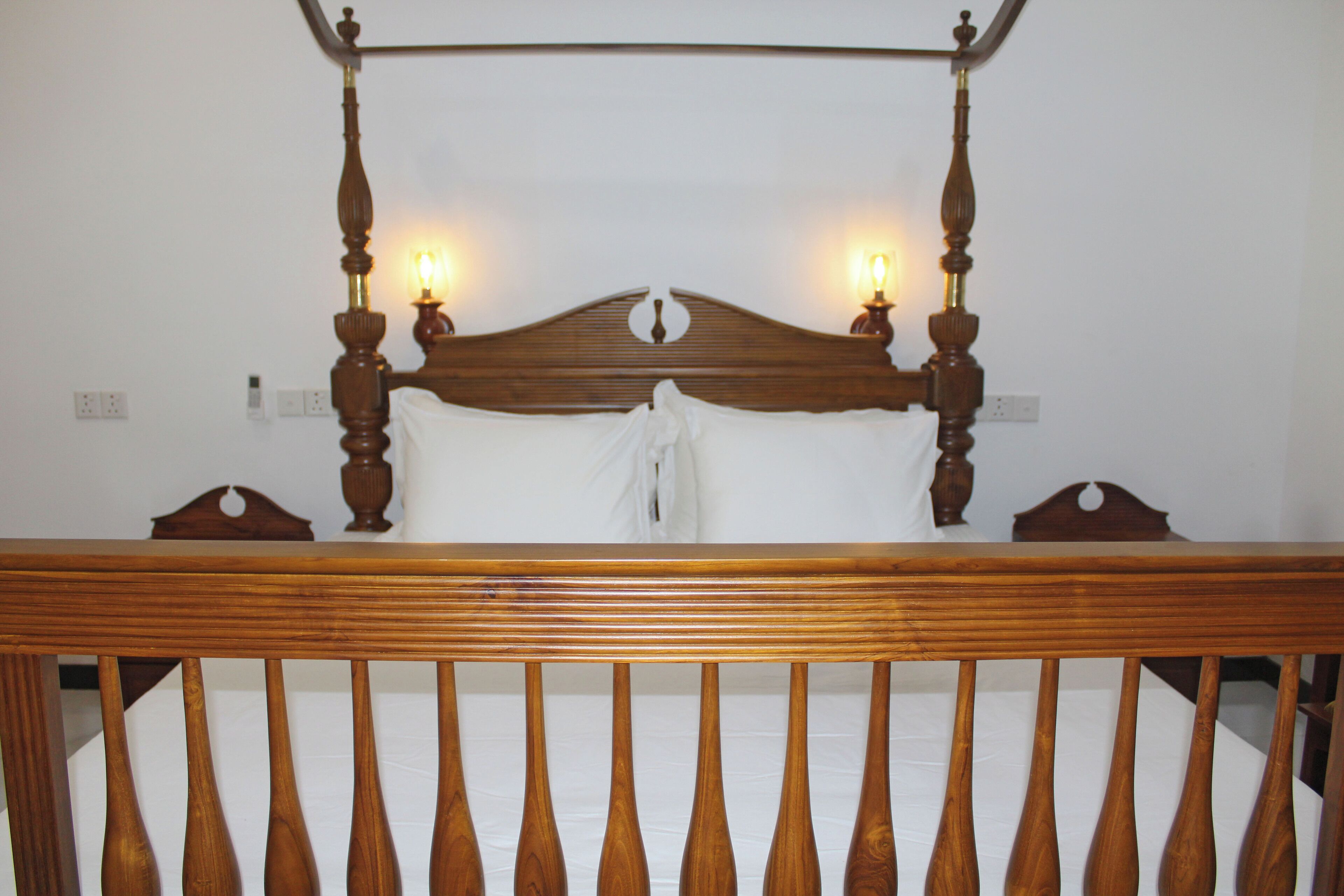 Una cama con dosel de madera, con un colchón blanco y dos mesitas de noche.