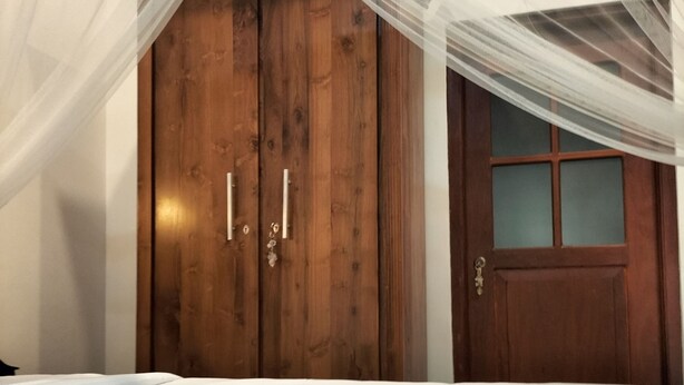 A bedroom with a canopy bed, wooden wardrobe, and a door with frosted glass panels. - Charika Villa (Bentota)