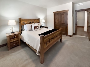 A wooden bed with a headboard featuring animal silhouettes, a bedside table with a lamp, and a door in the background.