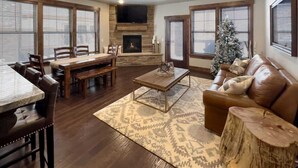 Una sala de estar con chimenea, televisor, árbol de Navidad y comedor.