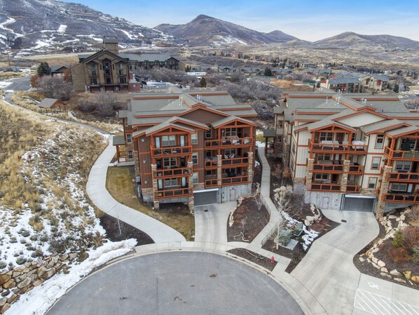 A multi-story building with a stone facade and large windows, surrounded by a landscaped area with a curved driveway and a snow-covered landscape in the background.