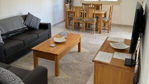 A modern living room with a black sofa, wooden coffee table, and dining table with chairs. - Stunning 3-bed Villa in Peyia (Pegeia)