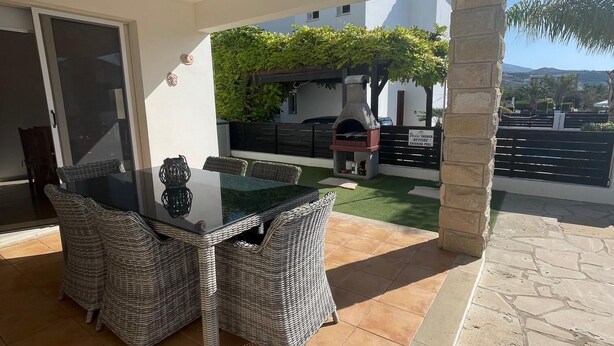 An outdoor patio with a glass-top table and wicker chairs, a stone pillar, and a stone-tiled floor. - Stunning 3-bed Villa in Peyia (Pegeia)