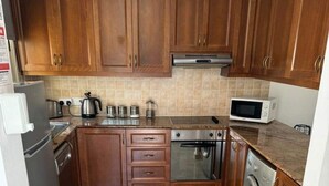 A compact kitchen with wooden cabinets, a stainless steel refrigerator, a microwave, a dishwasher, and a washing machine. - Stunning 3-bed Villa in Peyia (Pegeia)