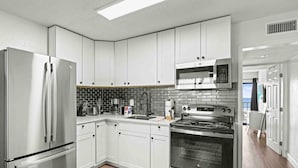A modern kitchen with white cabinets, stainless steel appliances, a black tiled backsplash, and a view to the outside.