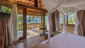 Una habitación con cama, televisión, sillón mecedora y vista a palmeras.