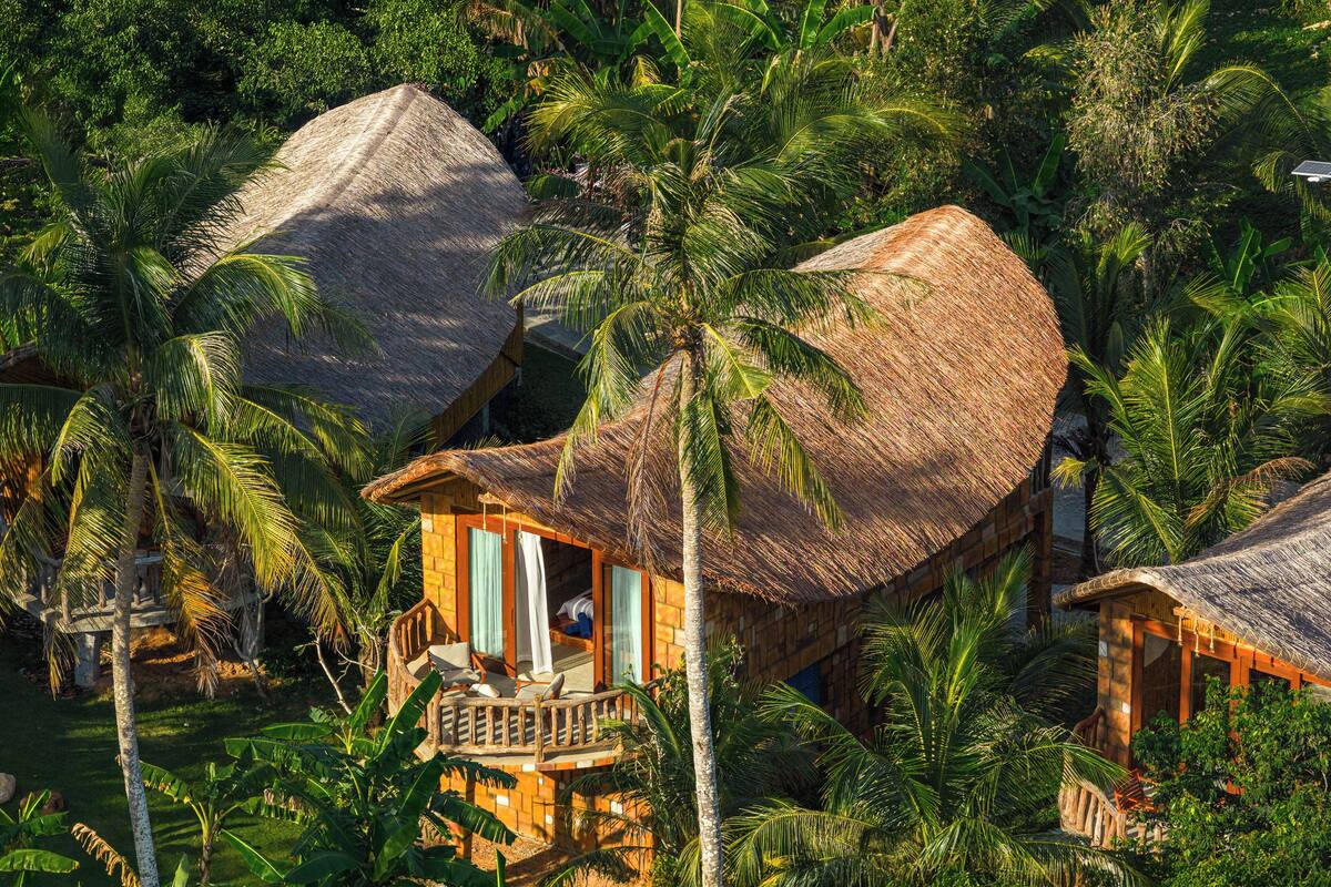 Un bungalow doté d’un toit de chaume, entouré d’une végétation tropicale luxuriante.