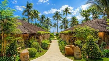 A pathway leading to a row of thatched-roof huts surrounded by lush greenery and palm trees.