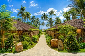 A pathway leading to a row of thatched-roof huts surrounded by lush greenery and palm trees.