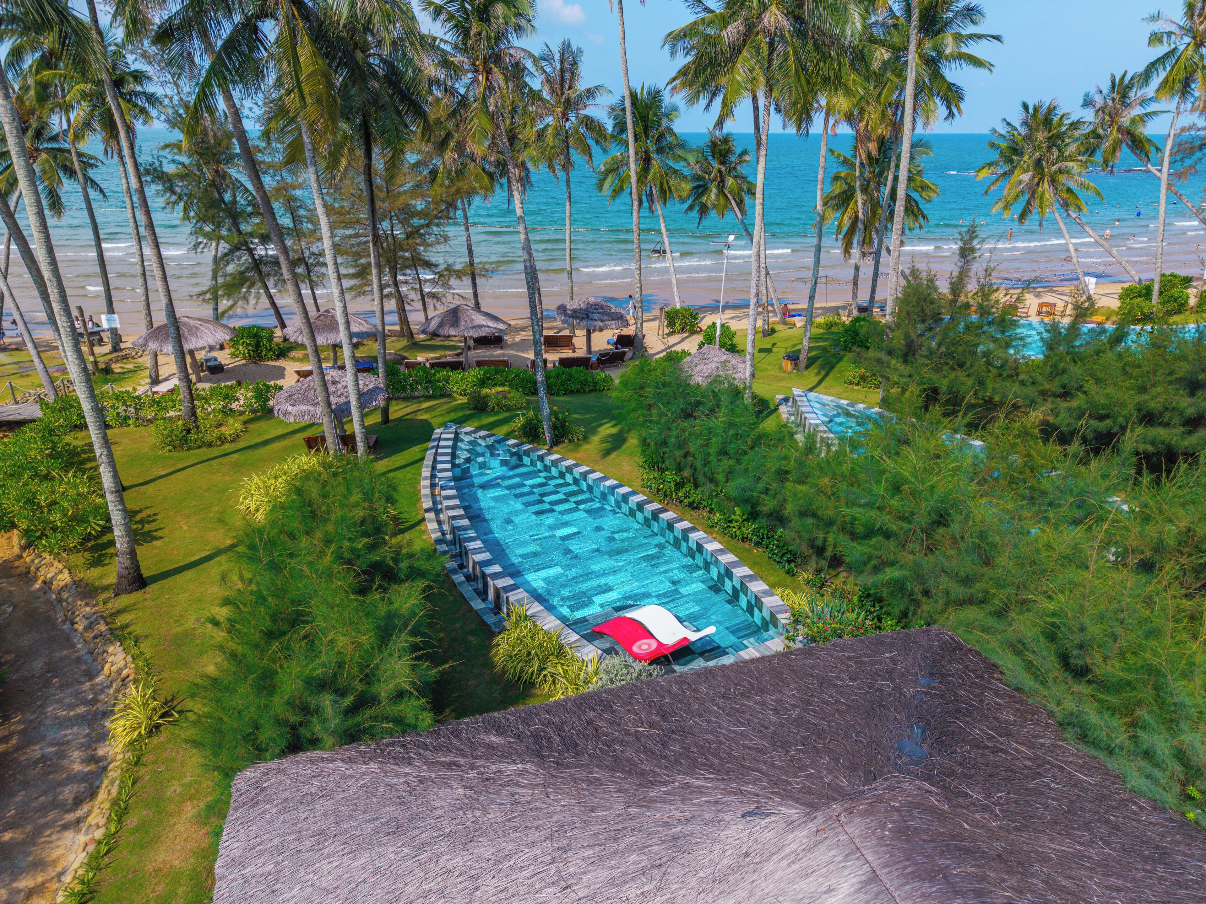 A swimming pool with a red lounge chair, surrounded by palm trees and a view of the beach.
