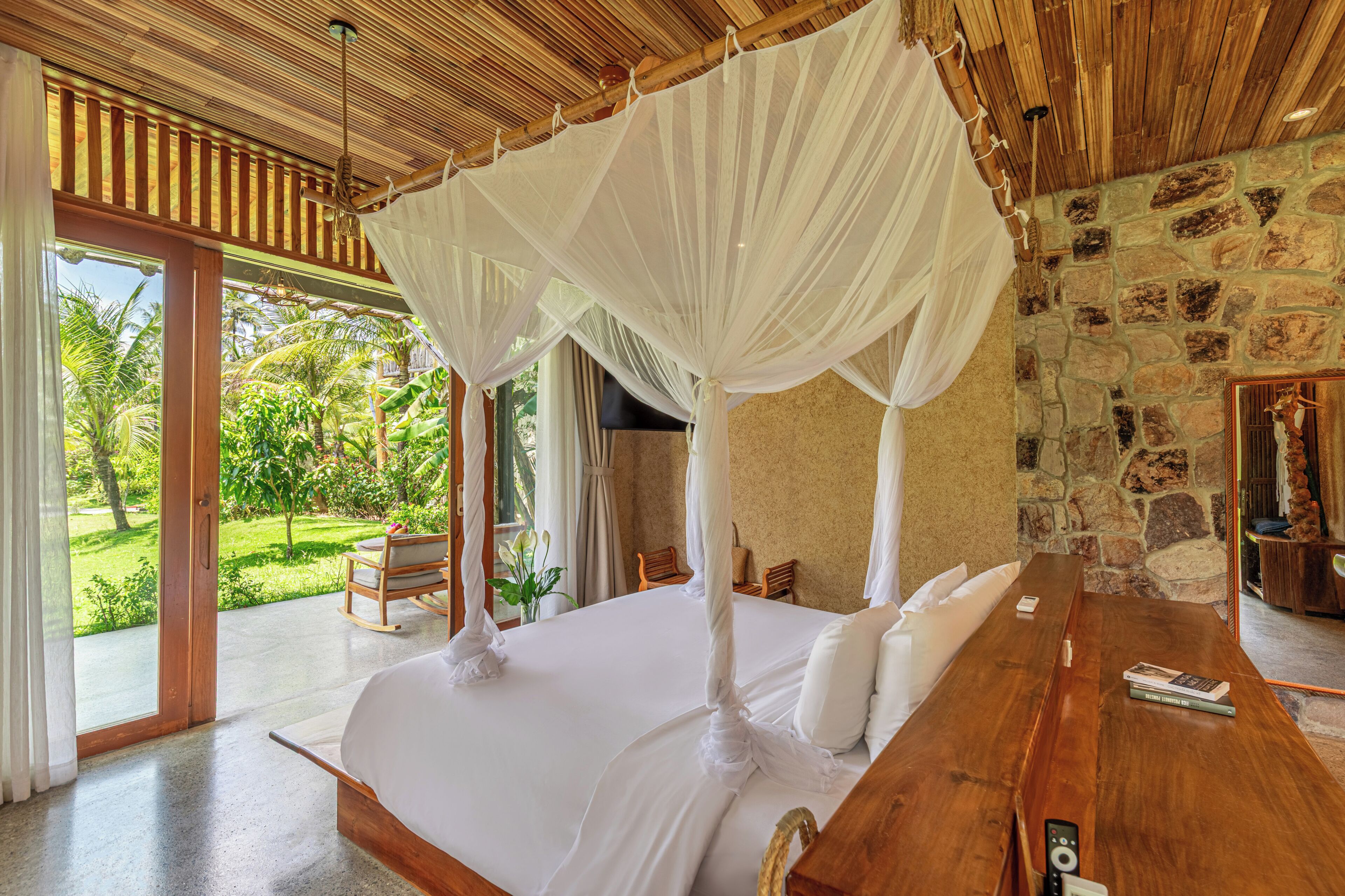 A room with a bed, a wooden table, and a stone wall.