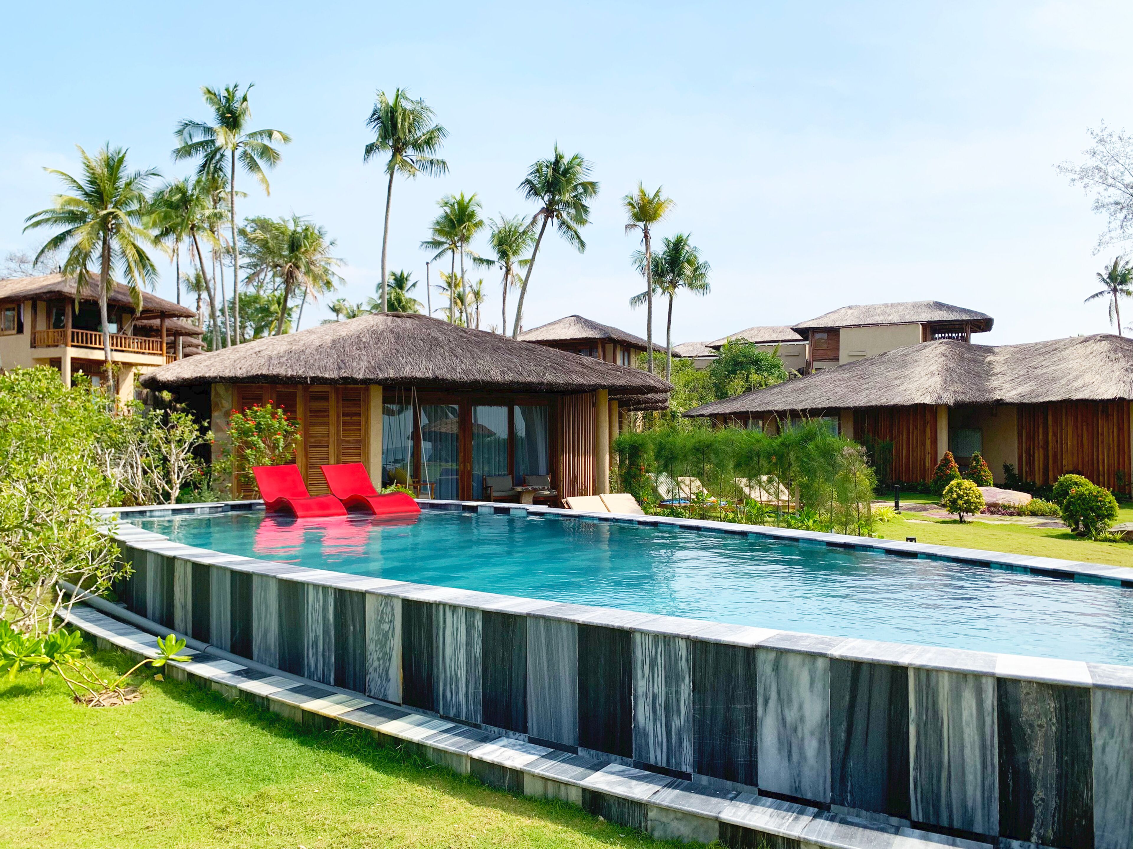 A resort with a swimming pool, thatched-roof structures, and lush greenery.
