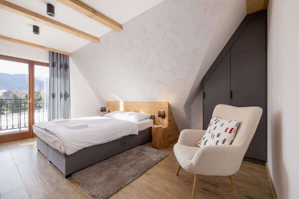 A bedroom with a bed, a chair, a nightstand, and a view of the outdoors.