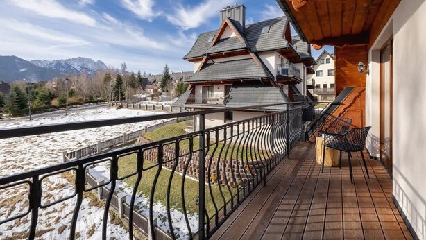 A balcony with a view of a mountain range, a wooden deck, and a chair.