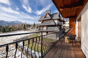 A balcony with a view of a mountain range, a wooden deck, and a chair.