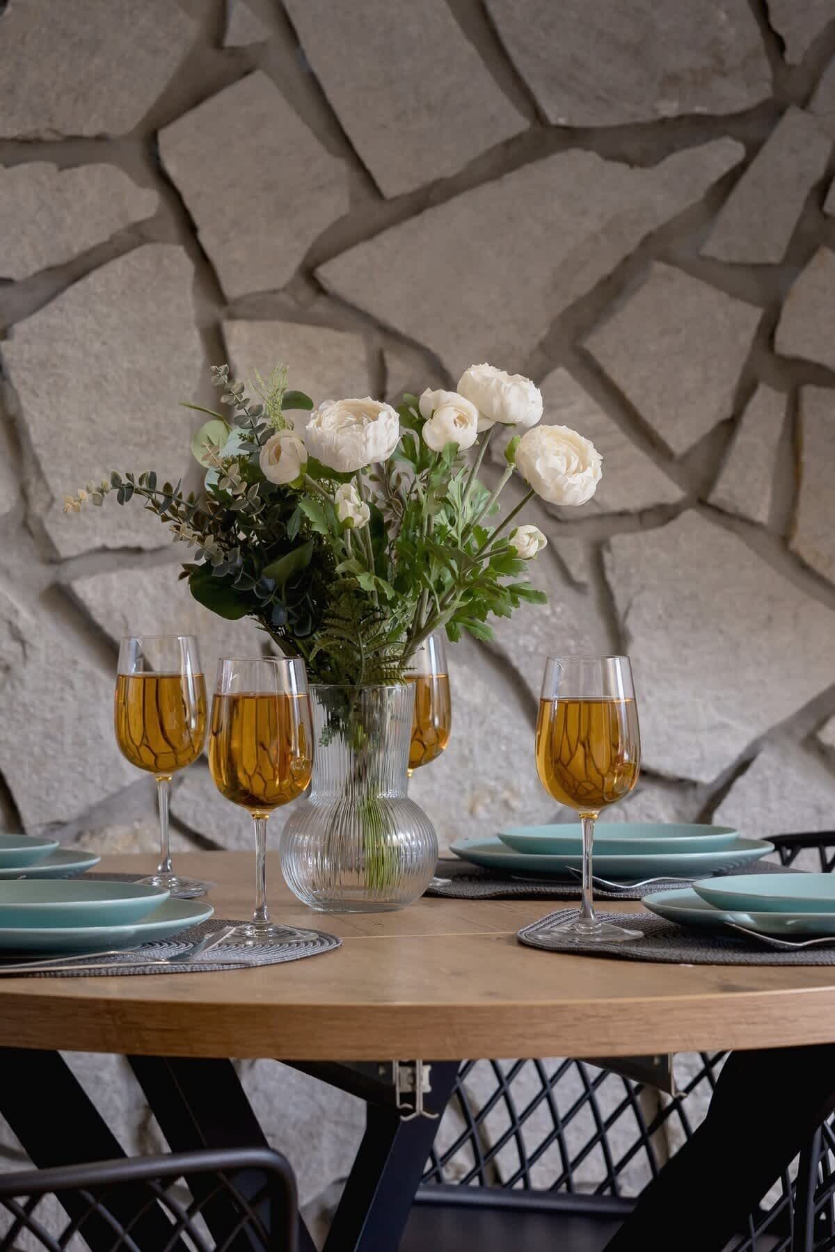 A table set with a vase of white flowers, four glasses of amber liquid, and teal plates and cutlery.