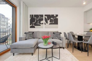 Un salon moderne avec un canapé gris, une table basse ronde et un coin repas avec des chaises grises.