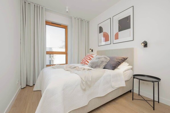 Une chambre moderne avec un grand lit, une table de chevet et une fenêtre avec des rideaux.