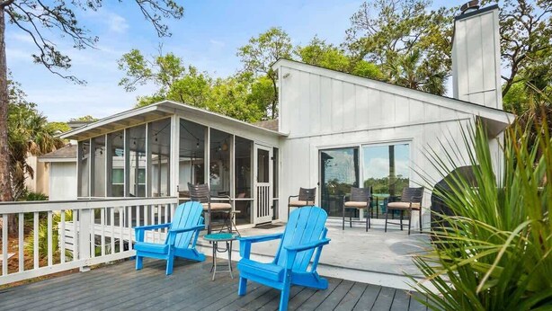 Une maison moderne dotée d’un patio couvert, d’un espace salon extérieur et d’une grande fenêtre donnant sur le paysage.