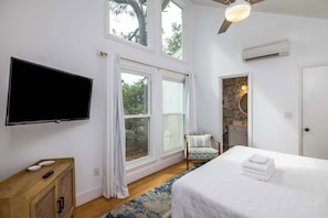 Une chambre à coucher avec un lit, une télévision, une chaise et de grandes fenêtres.