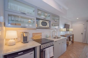 Cocina compacta con microondas, estufa y lavavajillas, alacenas con puerta de vidrio y un pequeño comedor.