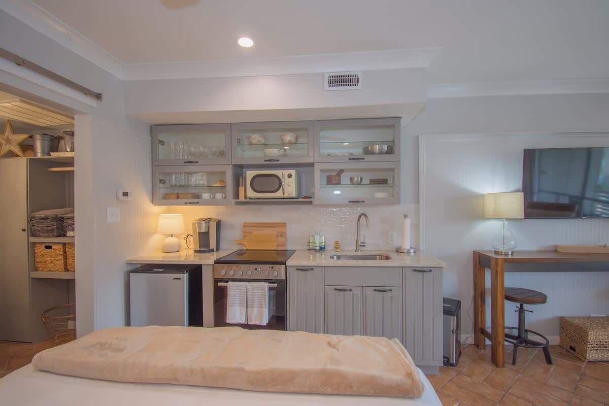 A compact kitchen with a microwave, stove, and sink, a small refrigerator, and a dining area with a table and chair.