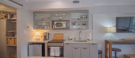 A compact kitchen with a microwave, stove, and sink, a small refrigerator, and a dining area with a table and chair.