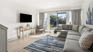 A modern living room with a flat-screen TV, a sofa, a coffee table, and a dining area with a table and chairs.