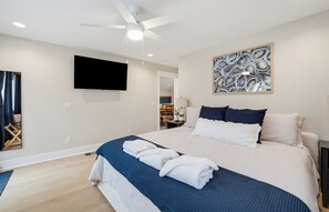 A hotel room with a bed, a ceiling fan, a flat-screen TV, and a wall-mounted artwork.