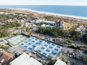 Vista aérea de una zona residencial costera con una gran cancha de tenis, acceso a la playa y una piscina.
