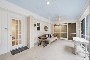 A room with a bed, a table, a ceiling fan, and a view through a glass door.
