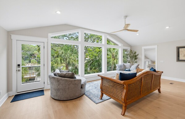 A spacious room with a high ceiling, large windows, a ceiling fan, and a wooden sofa.