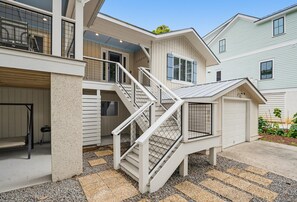A residential property with a multi-level structure, including a staircase with a metal railing, a garage, and a covered outdoor area with a gravel floor.