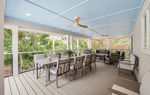 A covered outdoor patio with a dining table and chairs, a sofa, and a ceiling fan.